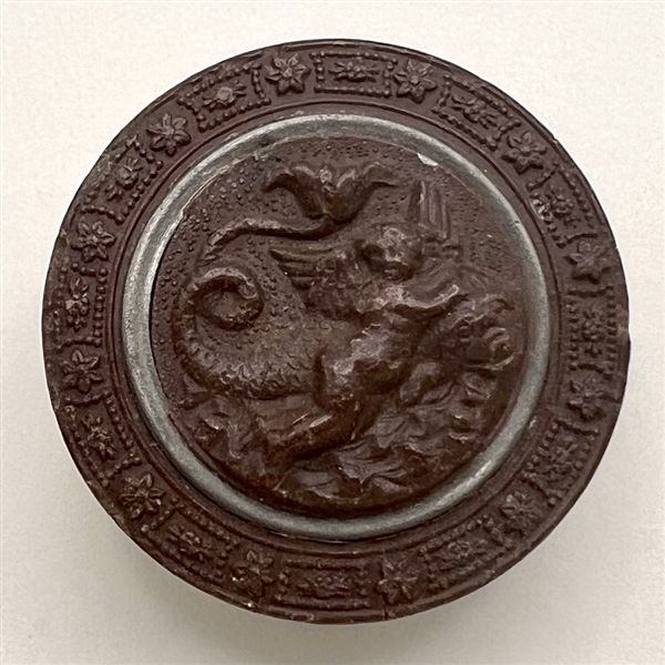 Gutta Percha button of cherub riding a dragon.