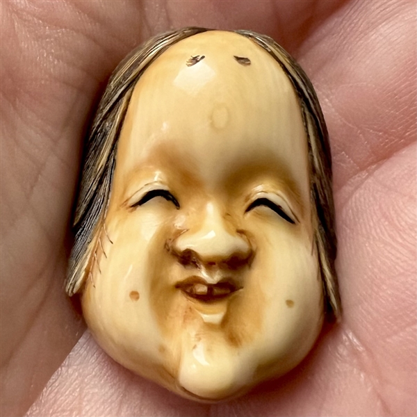 “Okame” moon-faced woman carved natural material netsuke.