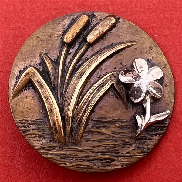 Stamped brass button of cattails and a flower.