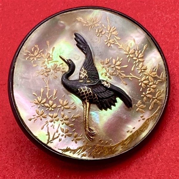 Incredible shakudo crane on iridescent pearl button with gold details of plant life.