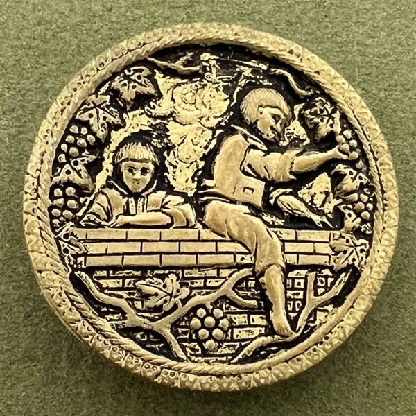 Stamped brass button of two boys on a wall picking grapes.