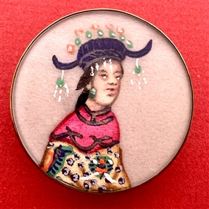 Painting on fabric button of a person in elaborate costume.