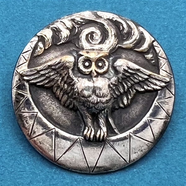 Silvered brass button of an owl over a crescent moon with clouds.