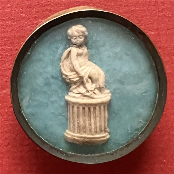 An 18th c. button of a cherub or putti on a pedestal.