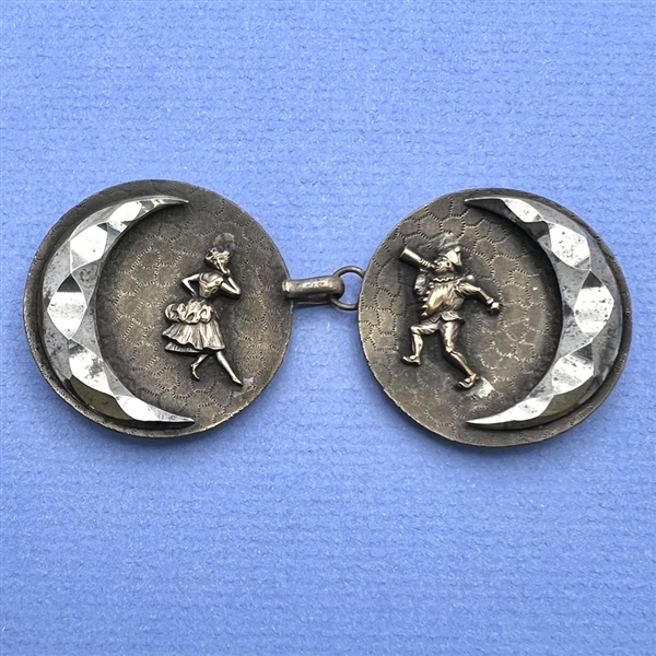 A button closure of brass with a woman and a jester and steel moons.