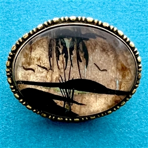 Reverse painted oval button of island scene with palm trees and flying birds.