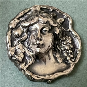 White metal button of a woman’s head with grapes.