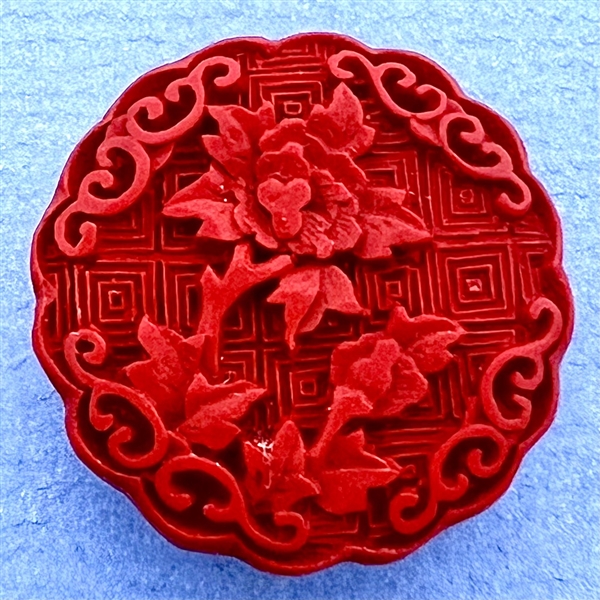 Modern “cinnabar” button of plant life over a background of squares.