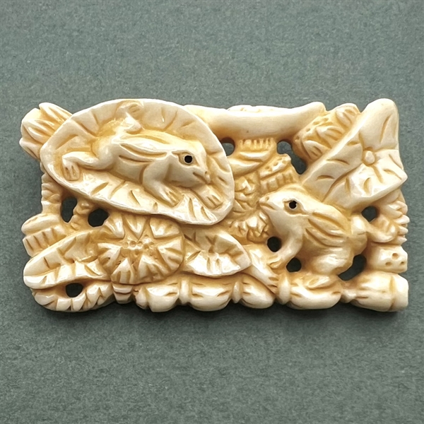 Carved natural material button of frogs and leaves.