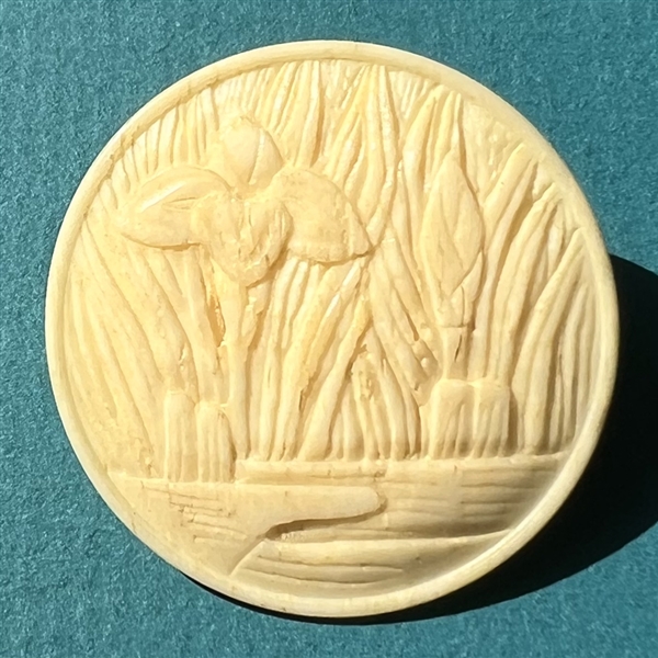 Carved natural material button of Japanese Iris among leaves.  