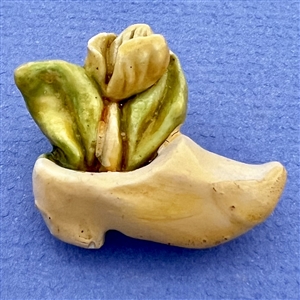 Painted plaster button of a clog holding a tulip.