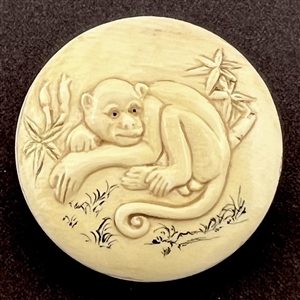 Carved natural material button of a monkey with plant life.