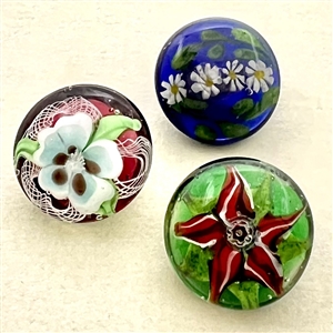 Three glass paperweight studio buttons of flowers.