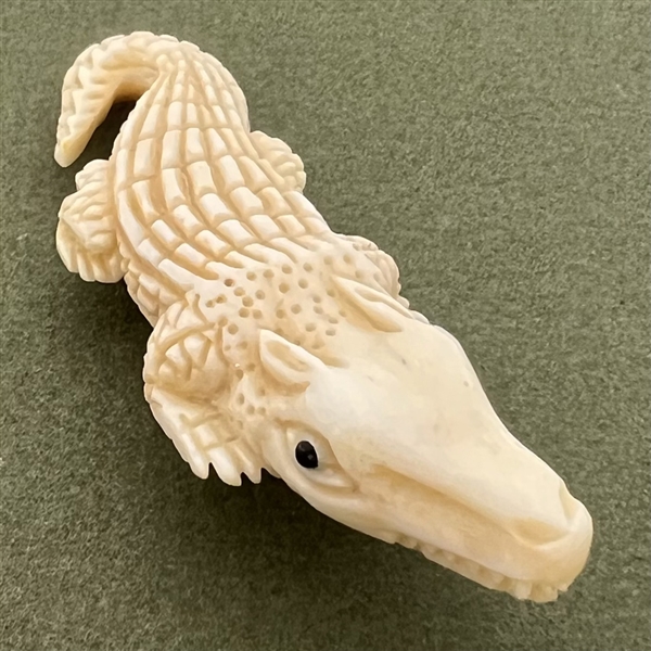 Carved natural material button of an alligator.