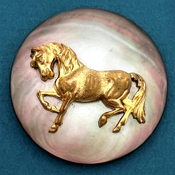 Gilded brass trotting horse over iridescent shell button.