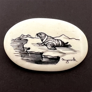 Scrimshaw button of a seal on top of ice on natural material.