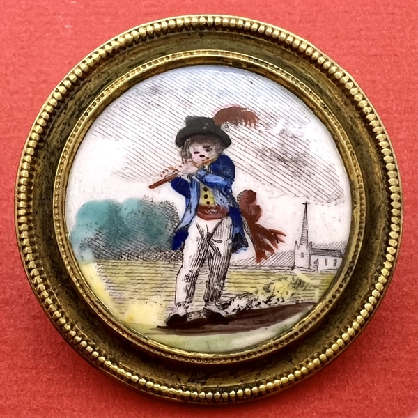 Painted porcelain button of a boy in blue playing a flute.