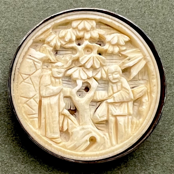 Carved natural material button of two Asian figures in a garden