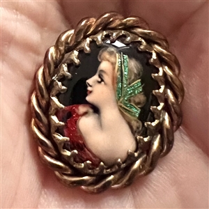 Oval enamel button with foil of a woman’s profile.