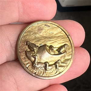 Brass button of ducks riding in a wooden clog boat.