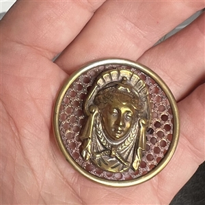 Brass screen back button of a royal woman's head.