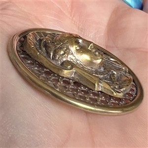 Brass screen back button of a royal woman's head.