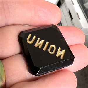 Modified square black glass verbal button of the word “Union with the N's reversed.