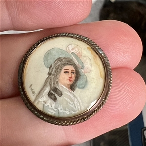 Painting on natural material button of woman in blue hat.