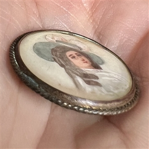Painting on natural material button of woman in blue hat.