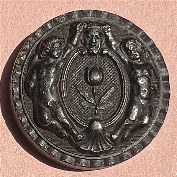 Horn button of putti holding horns of mask of Pan.