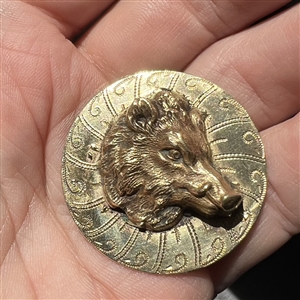 Brass button of a boar's head over a pattern.