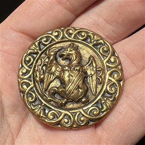 Brass button of a creature holding a shield. 