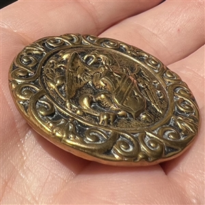 Brass button of a creature holding a shield. 