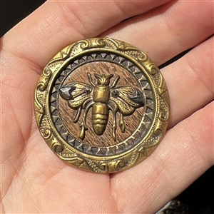 Brass button of a fabulous bee over a wood background. 