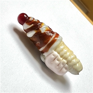 Mary Gaumond's torch-worked glass studio button of a twist ice cream cone held by a hand.