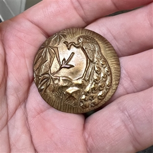 Brass button of a peacock near bamboo.