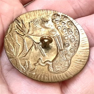 Brass button of a peacock near bamboo.