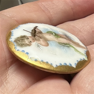 Painted porcelain button of a cherub playing a violin. 
