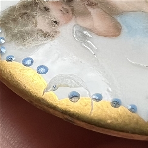 Painted porcelain button of a cherub playing a violin. 