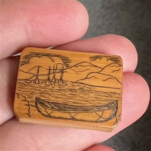 Wood studio pyrography button of a canoe and water scene.