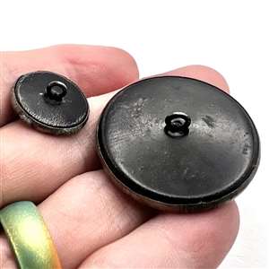 Two brass buttons in mother/daughter sizes of a potted plant on a wall. Or is it a ghost/love story?