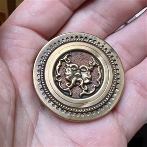 Brass Greenman button with a wood background.
