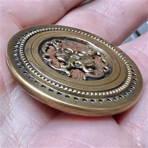 Brass Greenman button with a wood background.