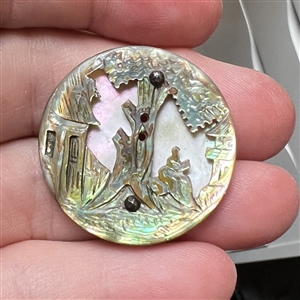 United carved abalone over lavender color shell button of a landscape scene.