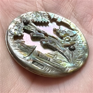 United carved abalone over lavender color shell button of a landscape scene.