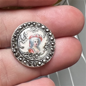 Enamel on white metal button of a woman in hat with border of faceted cut-steels.