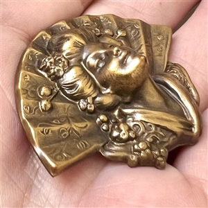 Stamped brass in high relief button of a realistic fan behind a Asian woman.