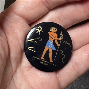 Painted casein button of an Egyptian man with symbols. 