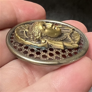 Brass screen back button of a royal woman's head.