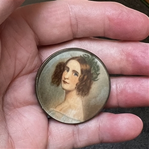 Painting of a woman on natural material under glass set in metal.